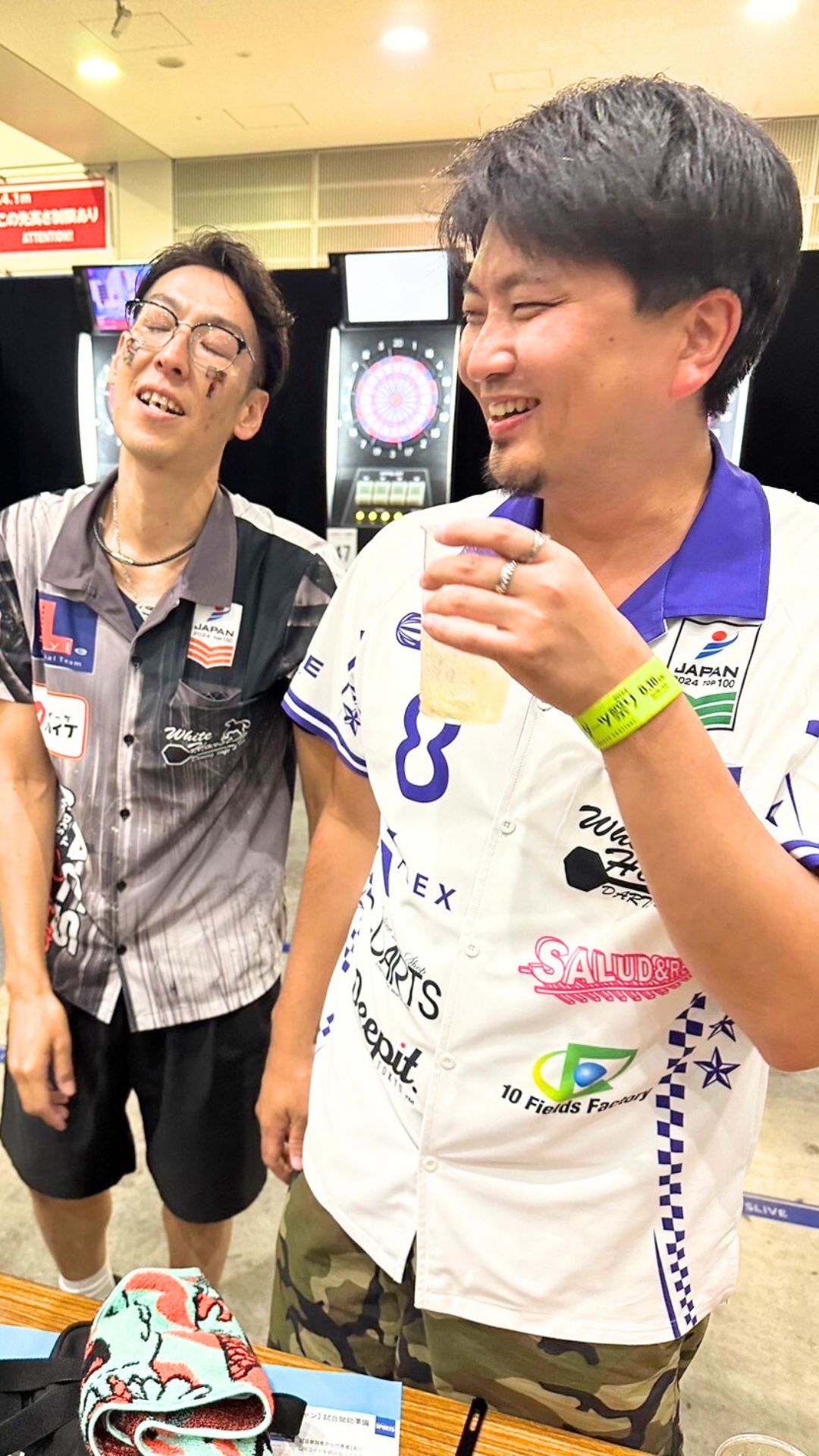 大会会場での風間佑太のオフショット。スポンサーロゴ入りユニフォーム姿で、ドリンクを片手に仲間とリラックスした笑顔を見せる。