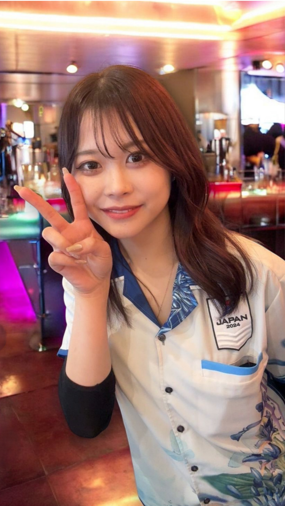 ダーツボードの前でピースサインをする女性プロダーツプレイヤー・内堀遥香さん