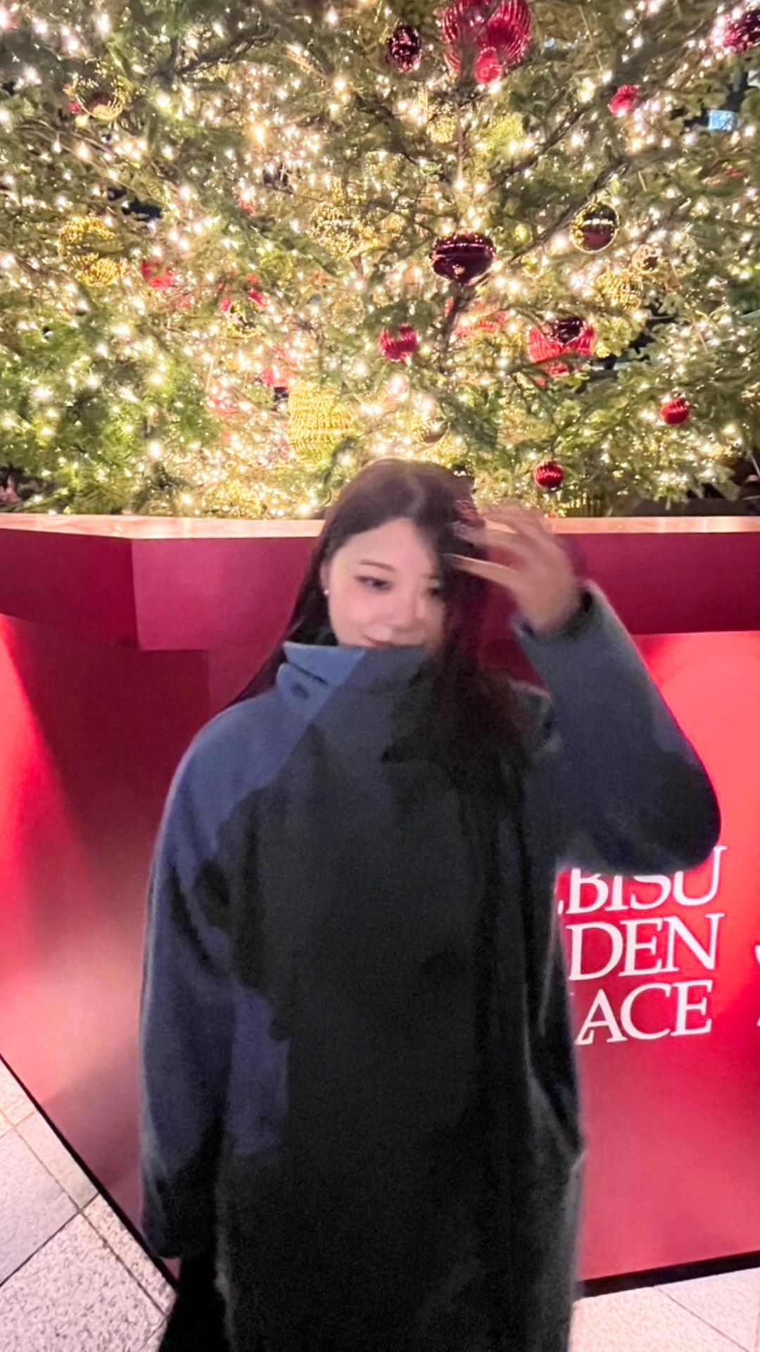 クリスマスツリーの前でほほえむ女性プロダーツプレイヤー内堀遥香さん。冬のイベント会場での一コマ