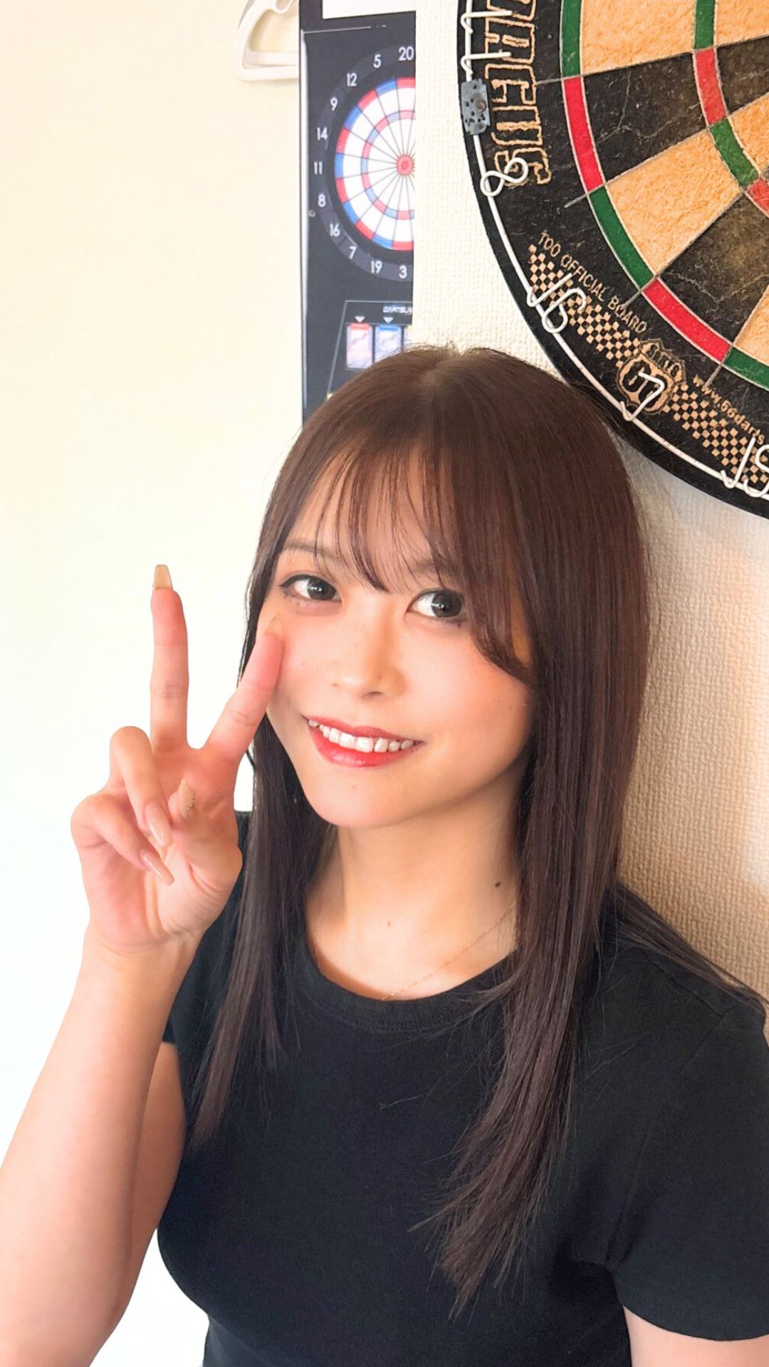 鏡越しにスマホで自撮りをする女性ダーツプレイヤー・カジュアルな私服姿