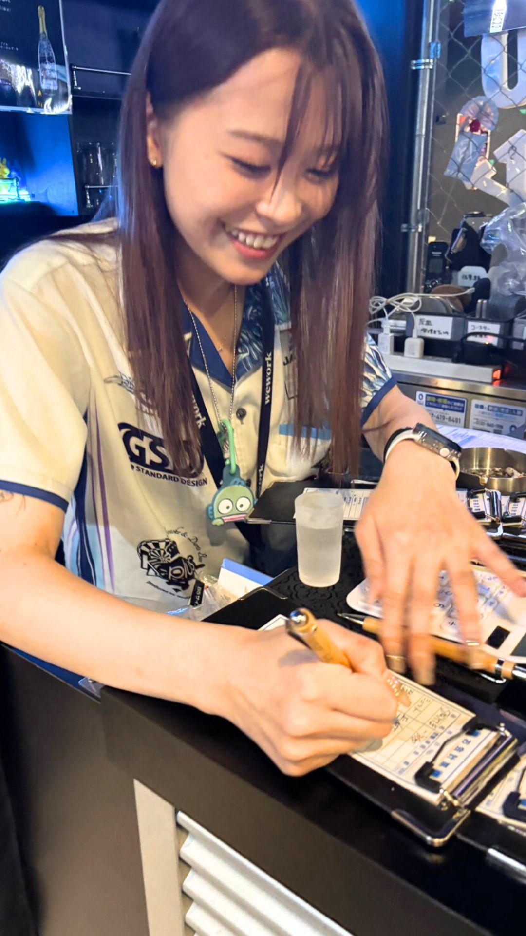 ユニフォーム姿で笑顔を見せる女性プロダーツプレイヤー内堀遥香さん。イベントでサイン中の和やかなシーン