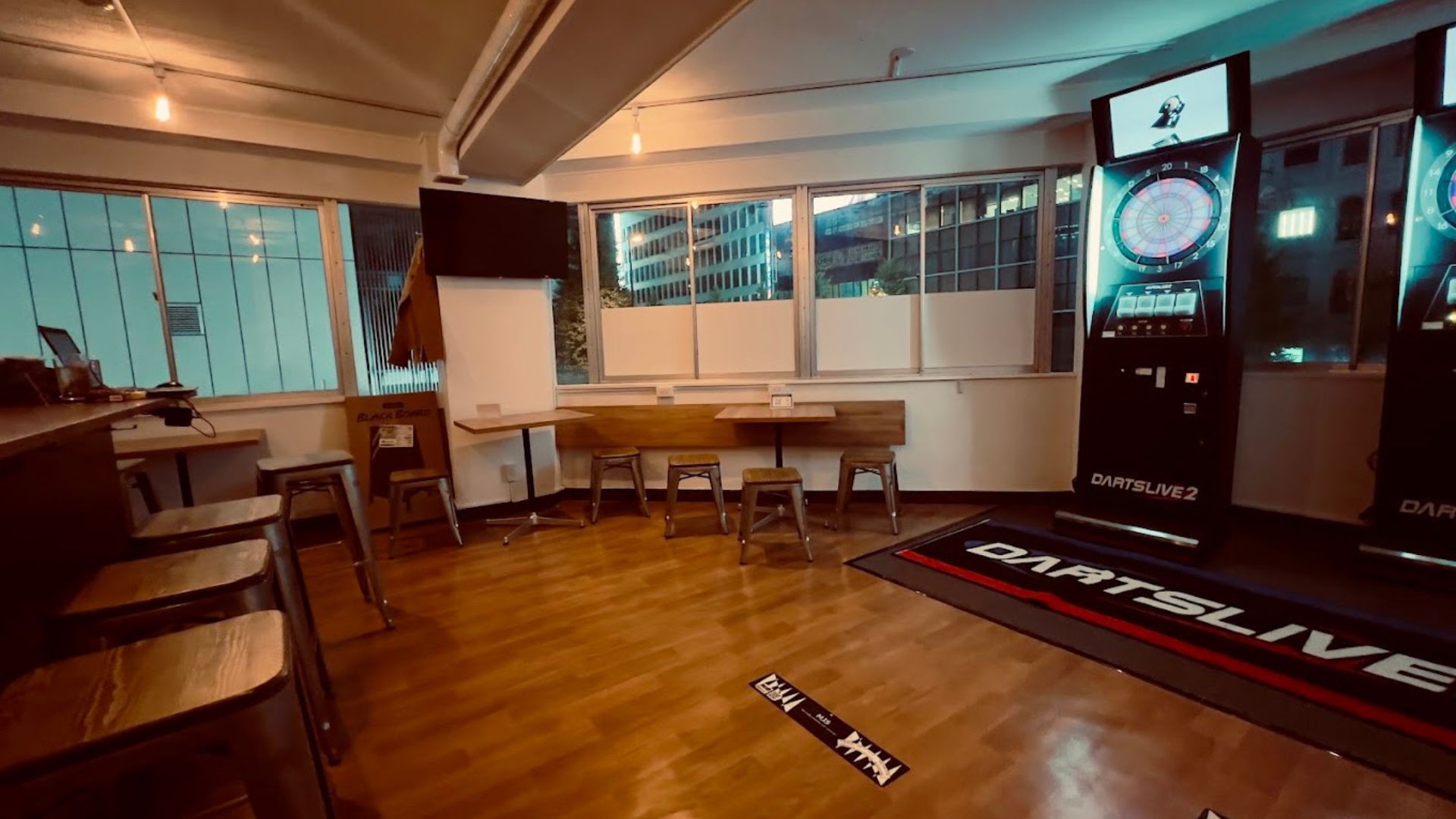 窓際にテーブル席が並び、奥にダーツライブが見える茶はいダーツバー西新宿Luuの店内