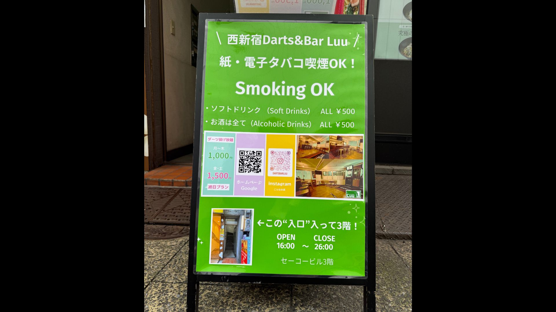 店舗前の立て看板。料金プランや営業時間、ビルの入り口がわかる外観写真。